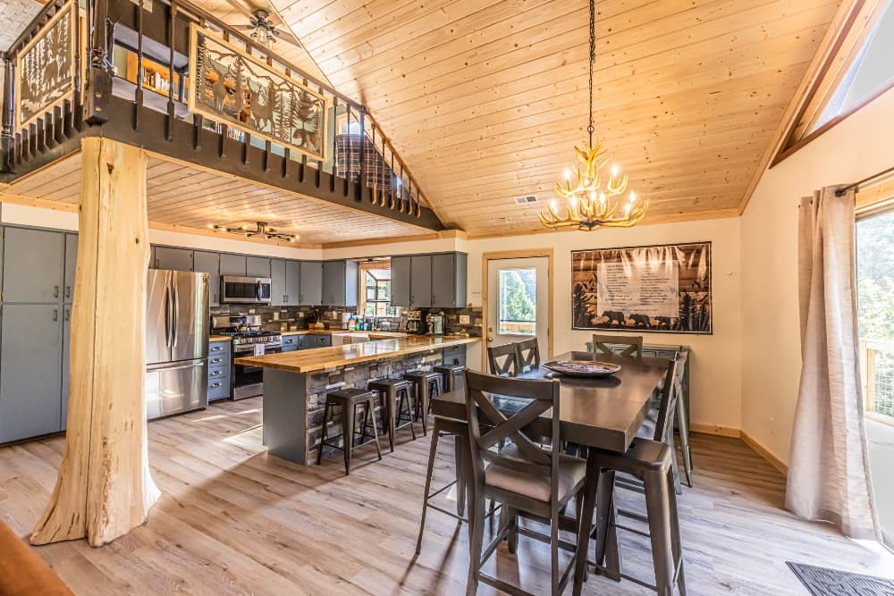Modern kitchen and dining area with wooden accents, large windows, and an upper loft.
