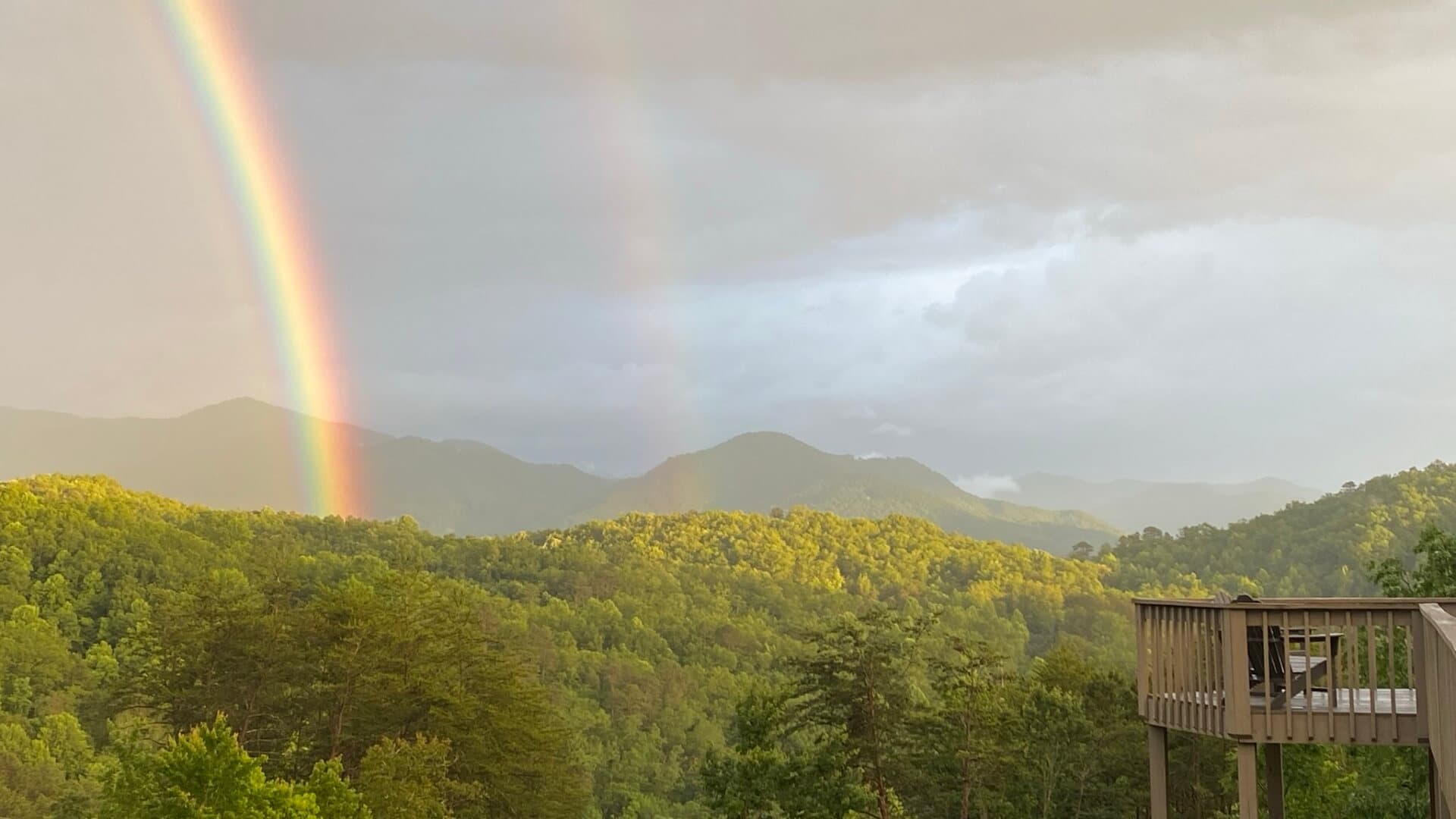 A vibrant rainbow arcs over green mountains after a rainstorm.