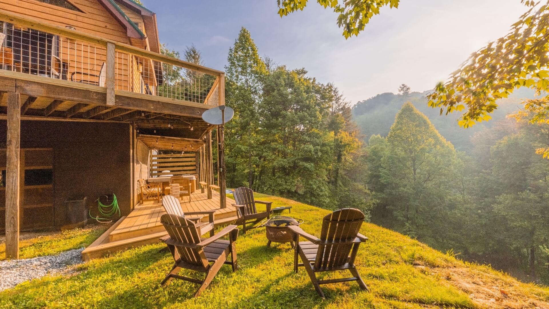A cozy cabin deck with wooden chairs overlooking lush green hills at sunrise.